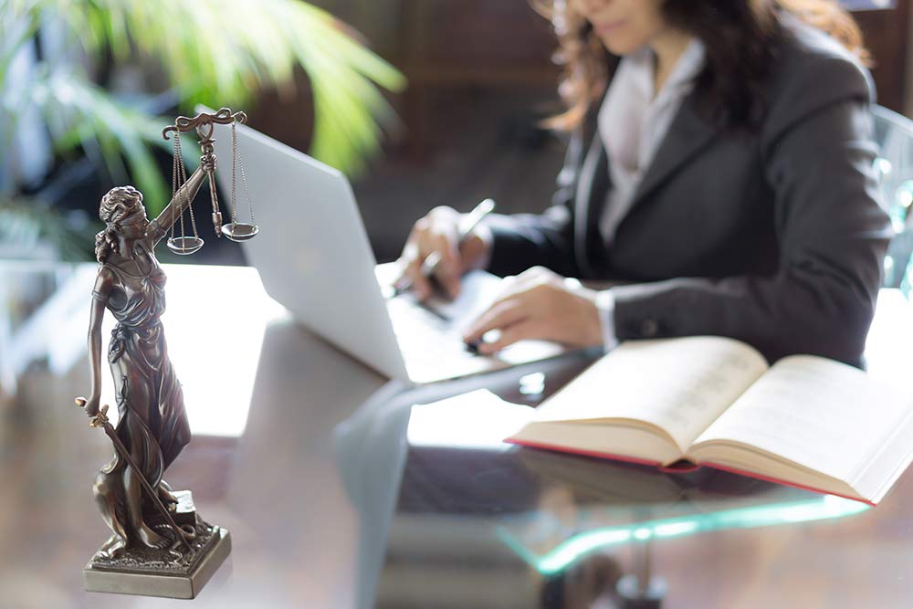 Justitia figure on desk, woman with computer